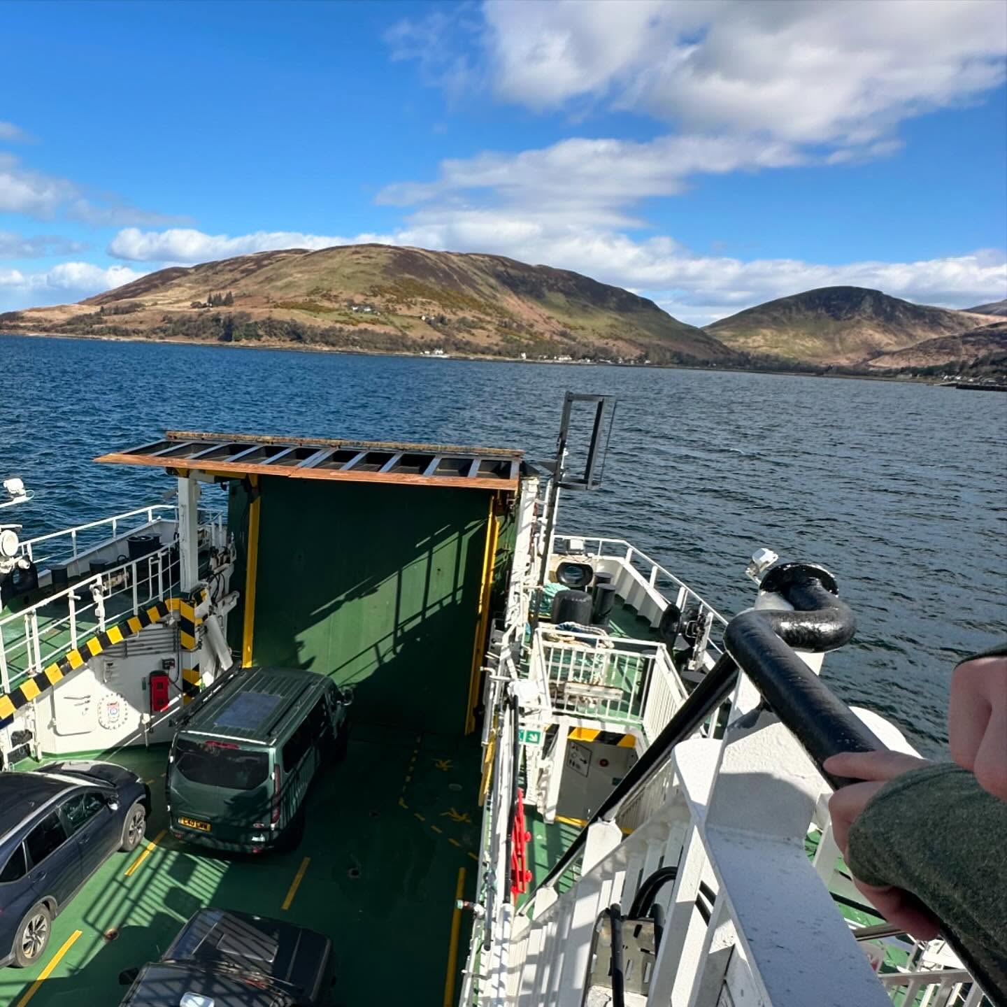 Cars on a ferry deck with water and hills beyond.