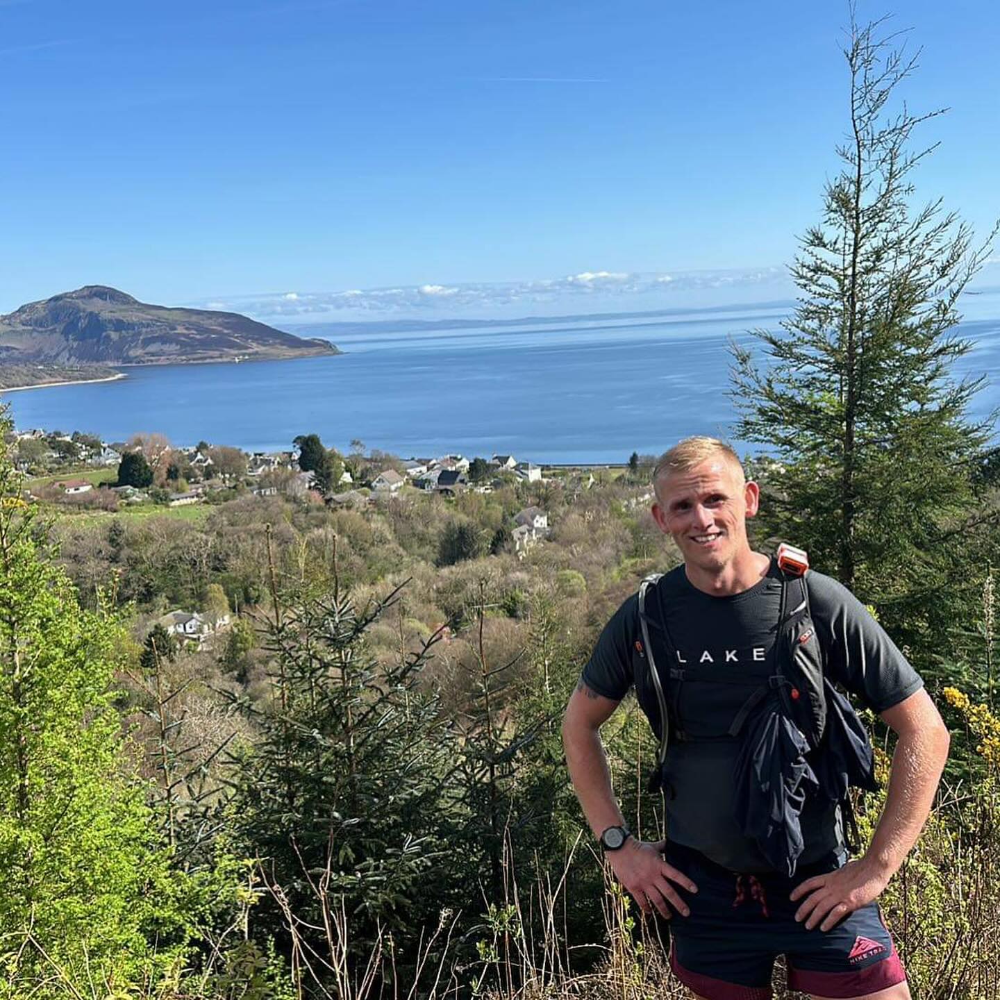 A runner on a wooded hillside overlooking a bay.