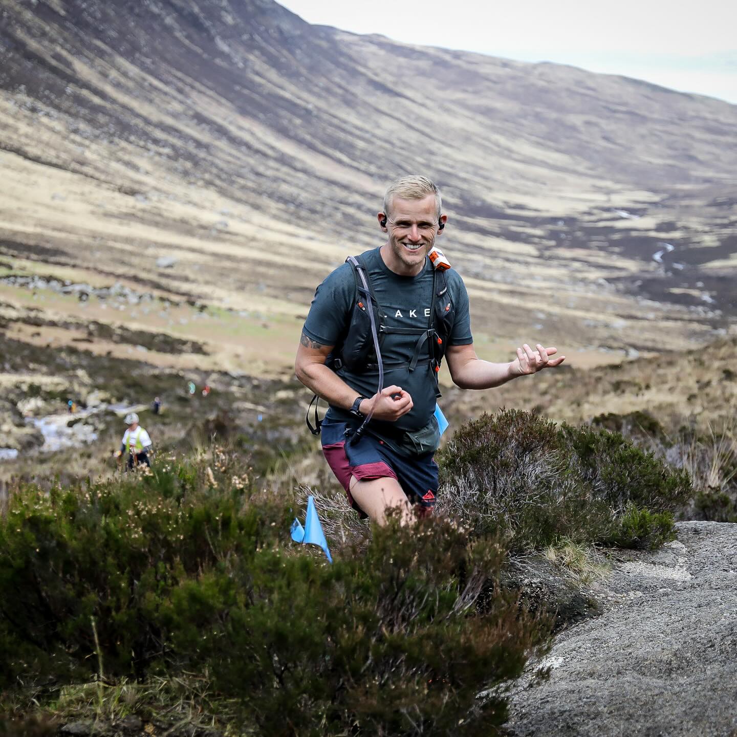 A runner climbing a rocky trail with an open mountain valley behind.