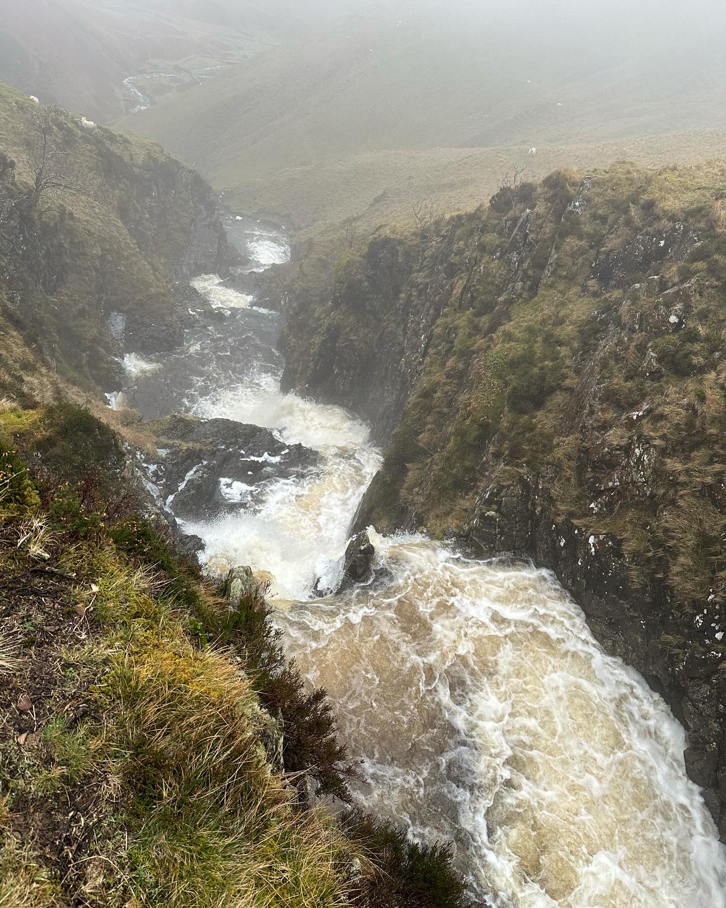 Water rushing down a steep rocky gully into the misty valley.