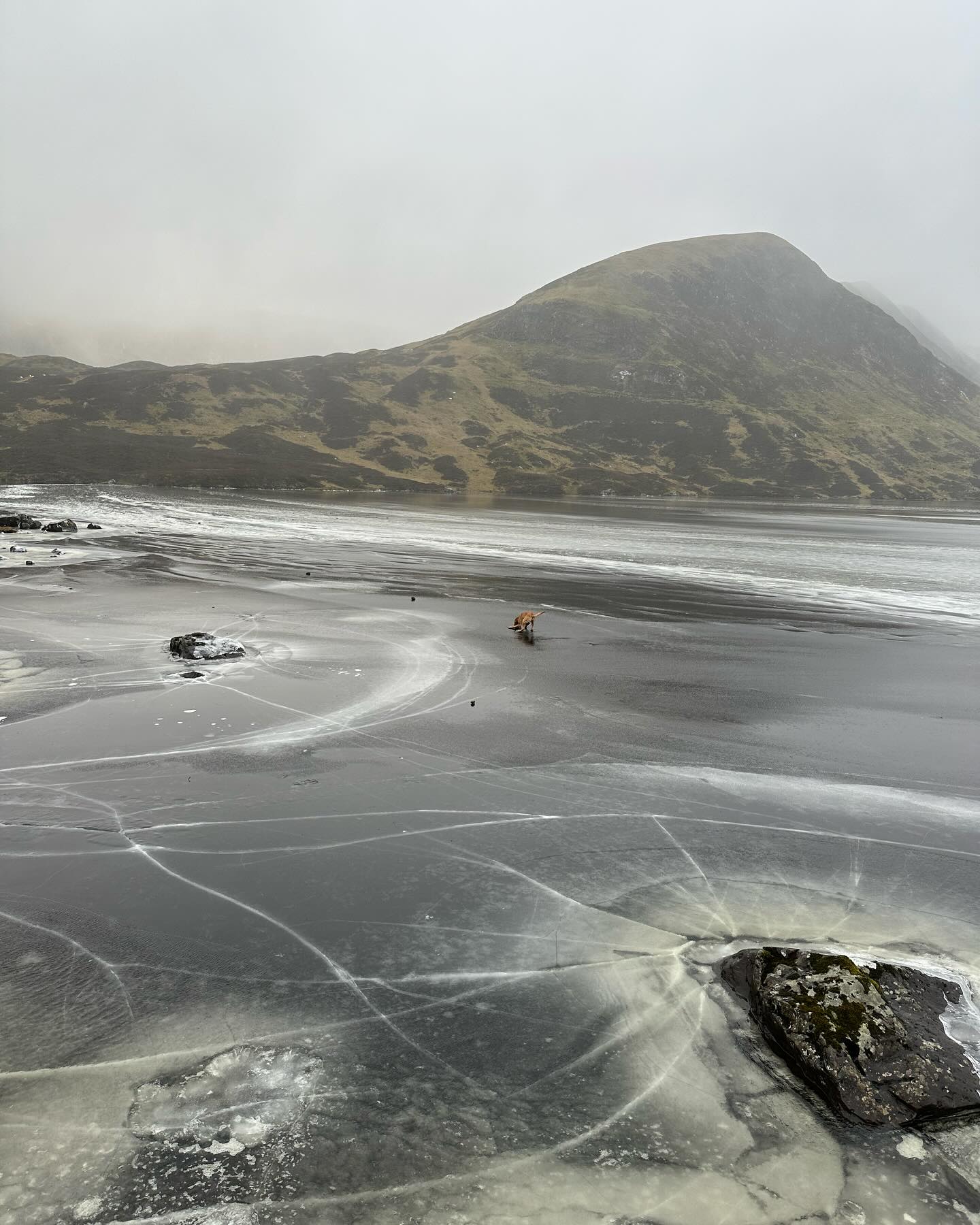 Ice across the loch beneath a mist-covered hillside.