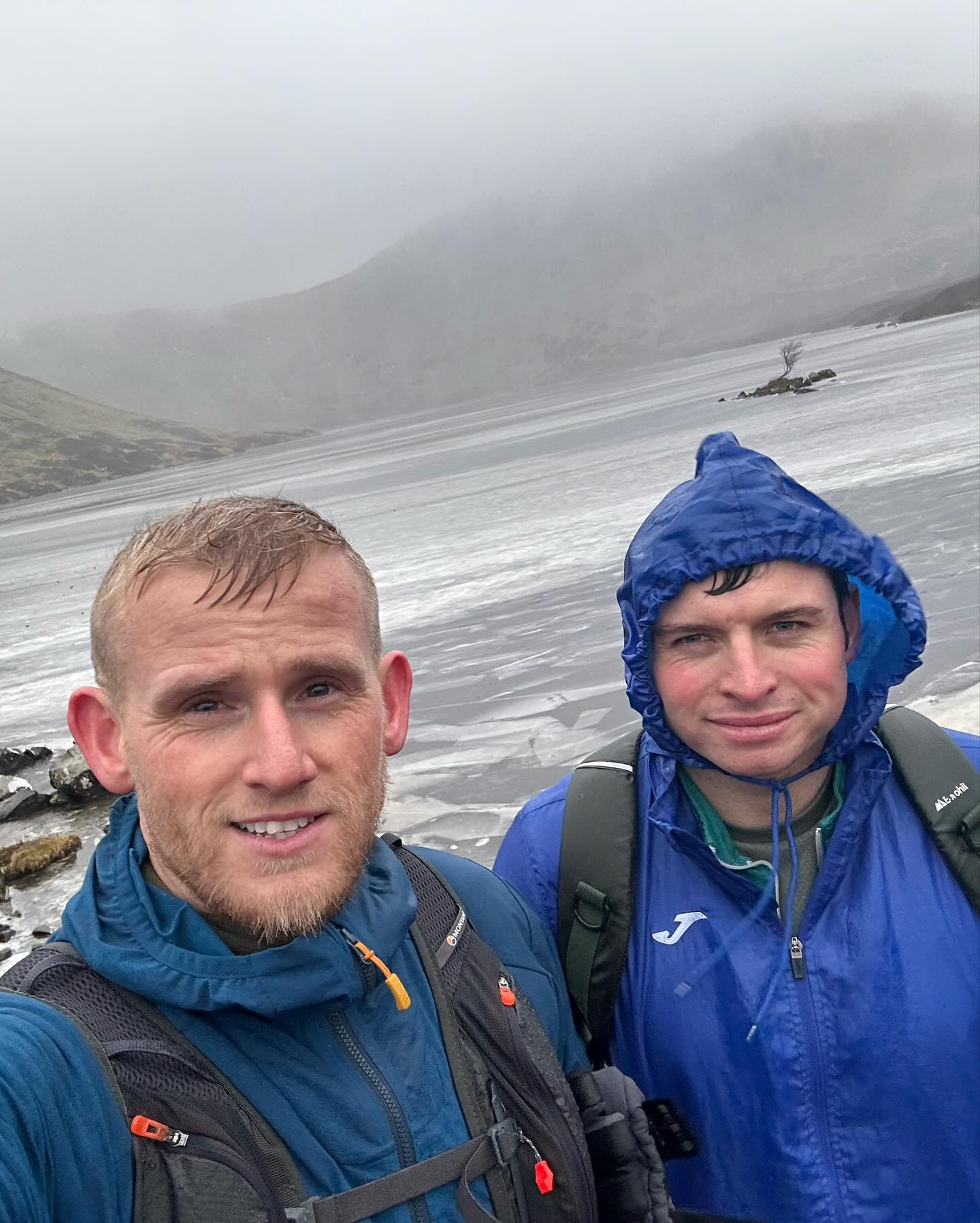 Two walkers in waterproof jackets beside an icy loch.