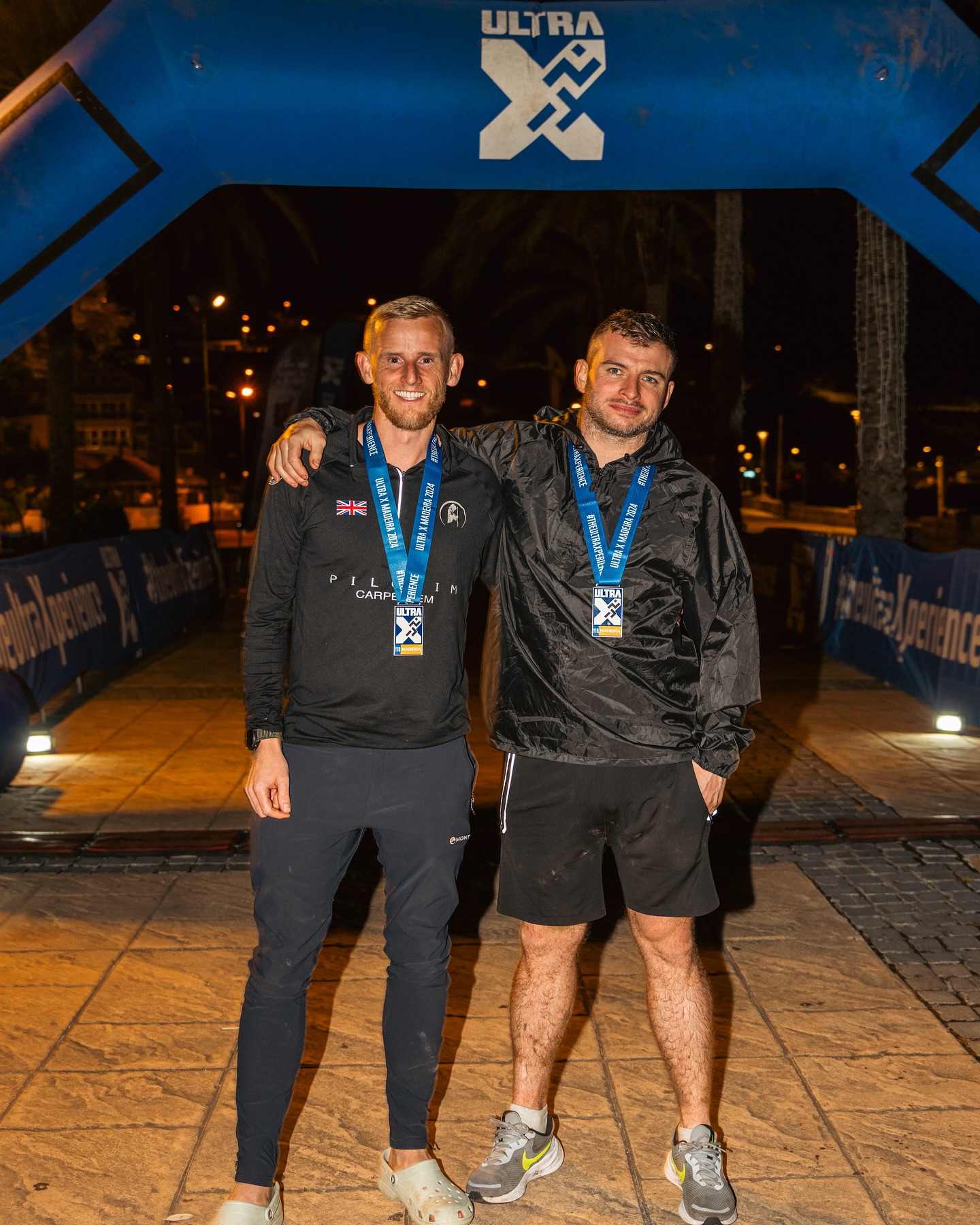 Two runners with finisher medals beneath the Ultra X Madeira finish arch.
